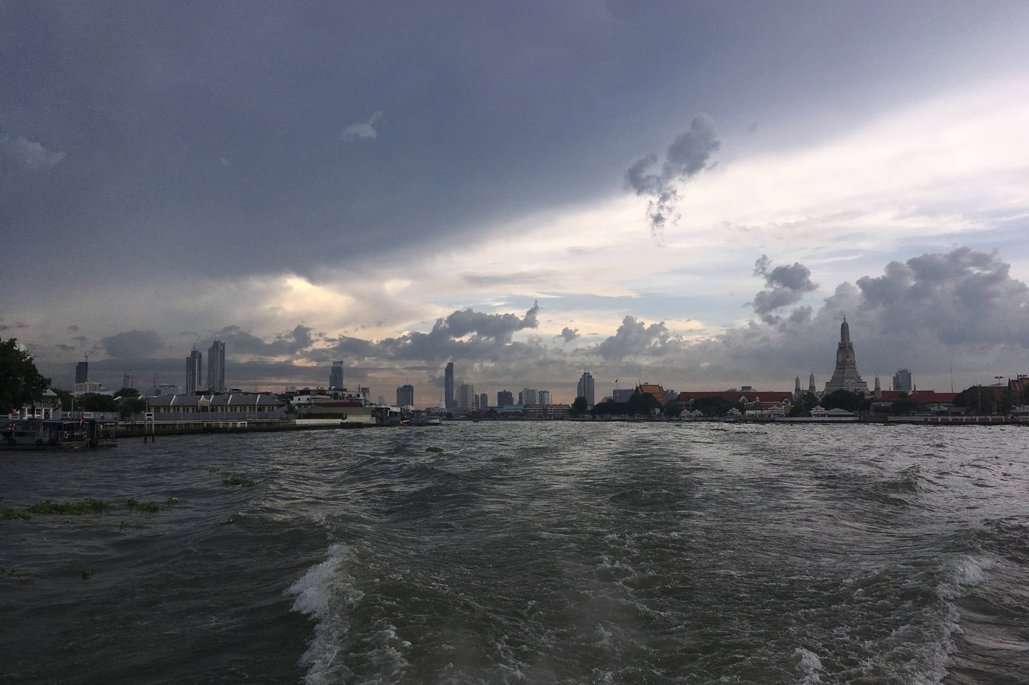 The Chao Phraya River in Bangkok at dusk, seen from a river boat with the spire of Wat Arun on the far bank